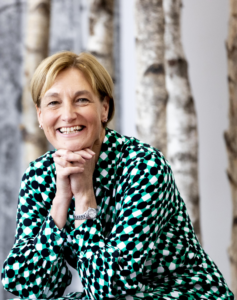 An image of Rebecca Cain wearing a green dress with a background of birch trees